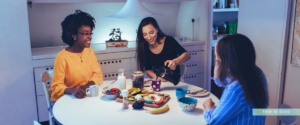 three women sitting around a dining table, sharing coffee and a meal in a bright, comfortable home environment
